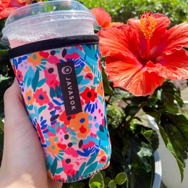 Hand holding a floral-patterned cup sleeve branded