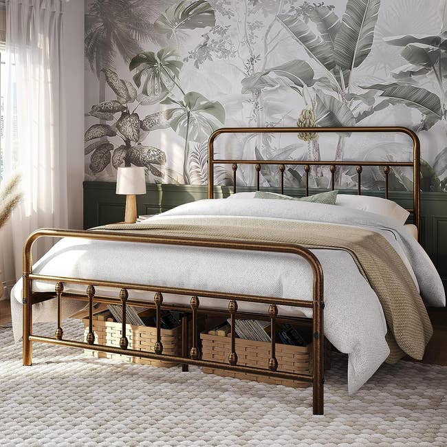 A metal-framed bed with white bedding, set in a room with tropical wallpaper, accompanied by wicker storage baskets underneath