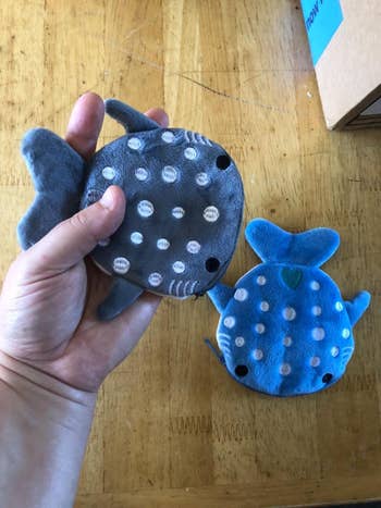 A hand holding one of two stuffed whale shark coin purses in grey and blue 