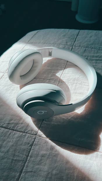 White over-ear headphones with a sleek design, resting connected a quilted surface, highlighted by brushed lighting. Ideal for tech-savvy shoppers