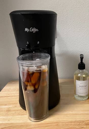 Reviewer image of black iced coffee maker with clear tumbler full of iced coffee on top of a wooden table