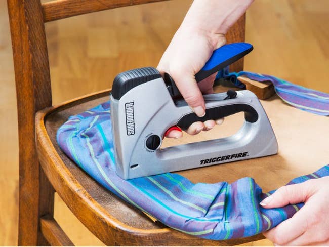 hand using the gun to staple fabric to wood