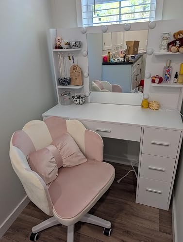 Vanity set with mirror and lights, pink cushioned chair, shelves with decor items and beauty products, in a well-lit corner of a room