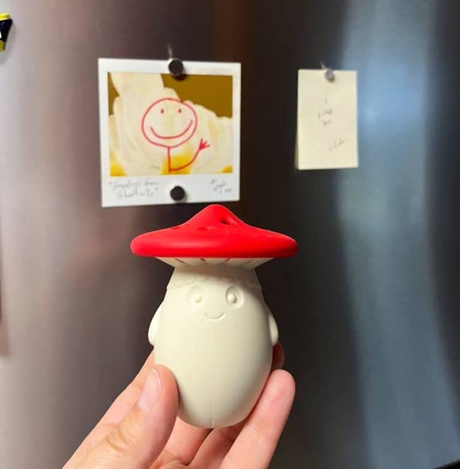 reviewer holding the fridge deodorizer, which looks like a smiling white mushroom with a red cap