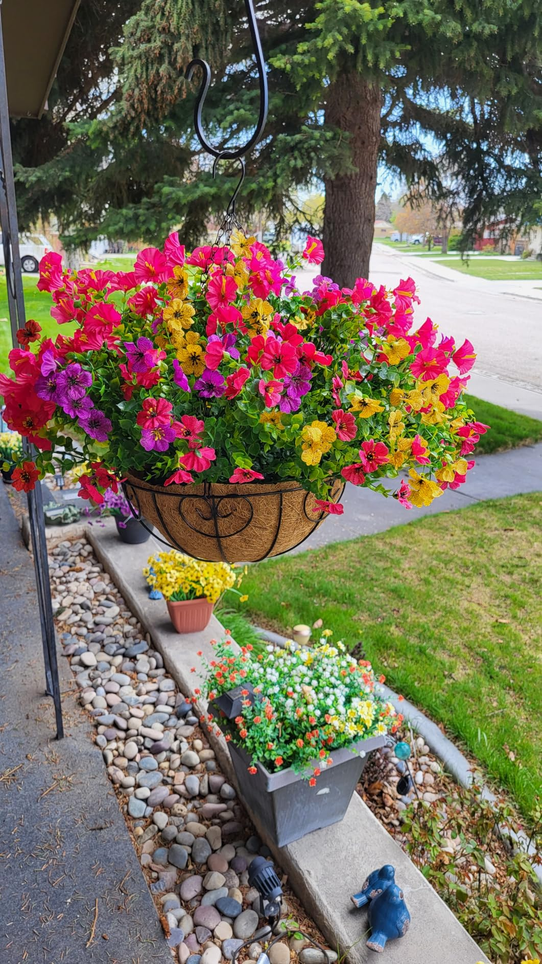Hanging planter overflowing with vibrant flowers connected  a porch, with much  angiosperm  pots below. Suitable for a location  plot  buying  article