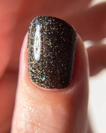 a thumb with a black glittery polish on it