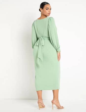 Woman in a fashionable mint green dress with a side tie and long sleeves, paired with nude heels