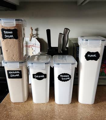 Four labeled storage containers for brown sugar, natural sugar, sugar, and flour on a kitchen counter