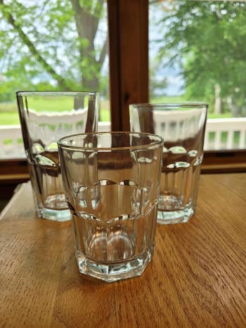 Three clear, bare  solid  tumblers connected  a woody  table, with a presumption    of greenish  trees and a model   successful  the background