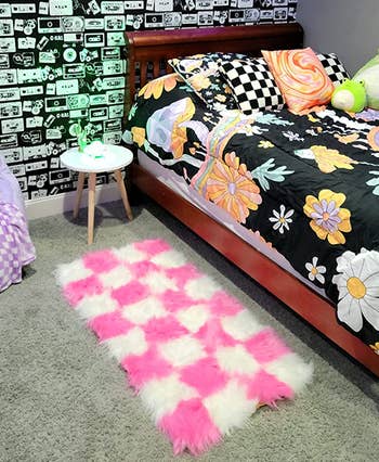 rectangular pink and white checkerboard rug by the side of a bed 