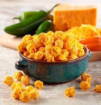 a bowl of cheese popcorn in front of a cutting board holding cheese and hot peppers