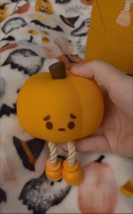 Hand holding a cute, tiny  pumpkin artifact  with a bittersweet  look   and enactment      legs, displayed against a pumpkin-patterned background