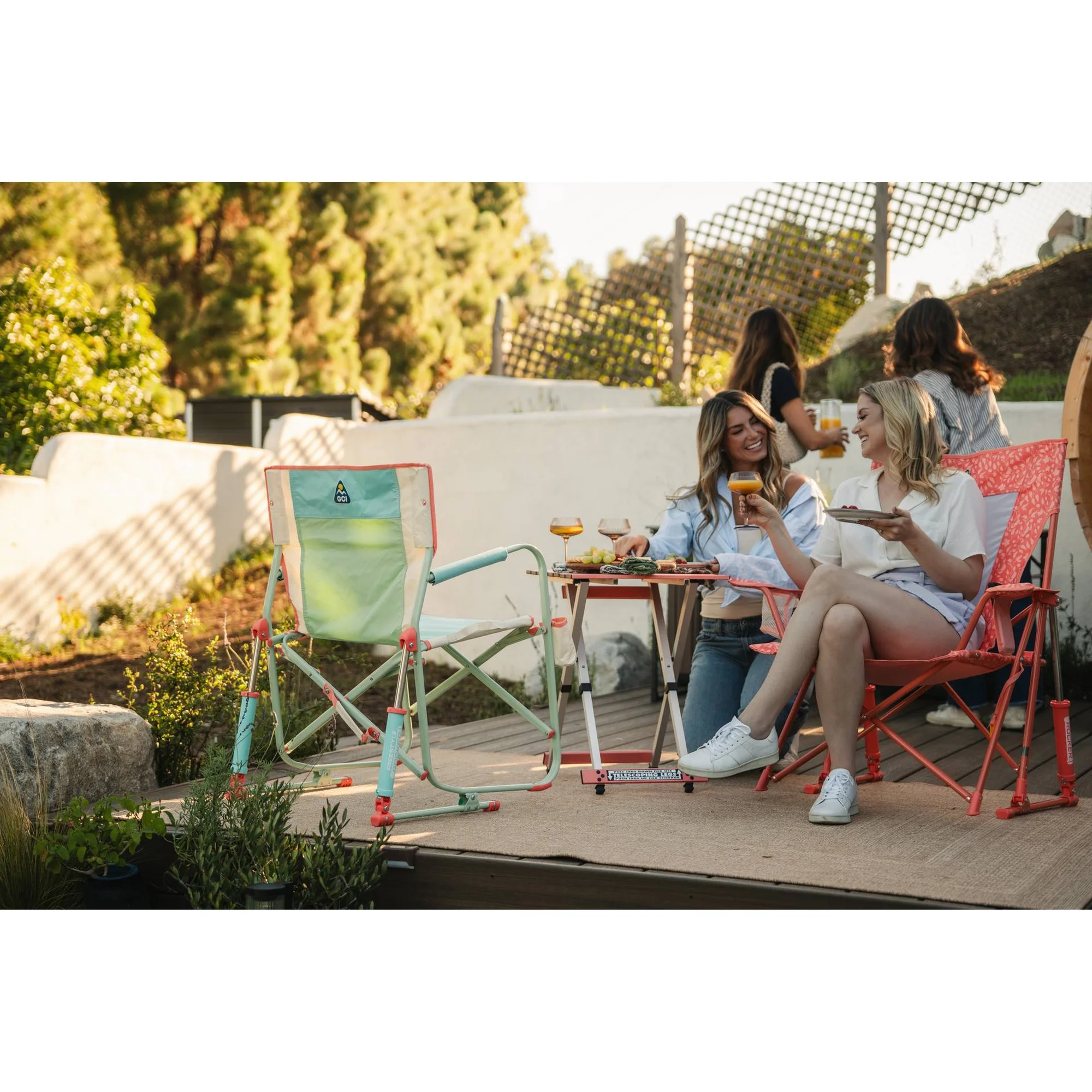People sitting outdoors successful  stylish folding chairs, enjoying a repast  with drinks and snacks connected  a table. Trees and greenery successful  the background