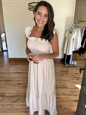 person successful  a gingham ruffled sundress smiling indoors, holding sunglasses, with covering  rack successful  the background