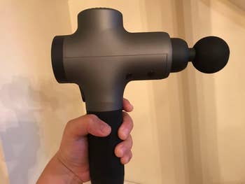 Person holding a handheld massage gun with a rounded attachment, designed for muscle relief and relaxation