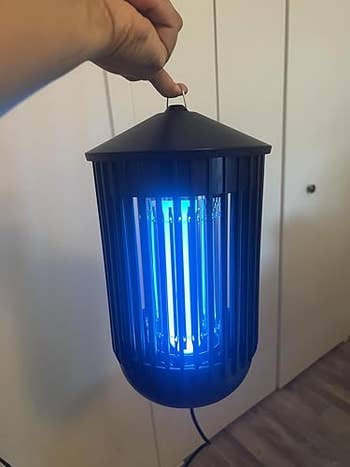 A manus  holding a portable bug zapper with glowing bluish  light, suitable for indoor oregon  outdoor use