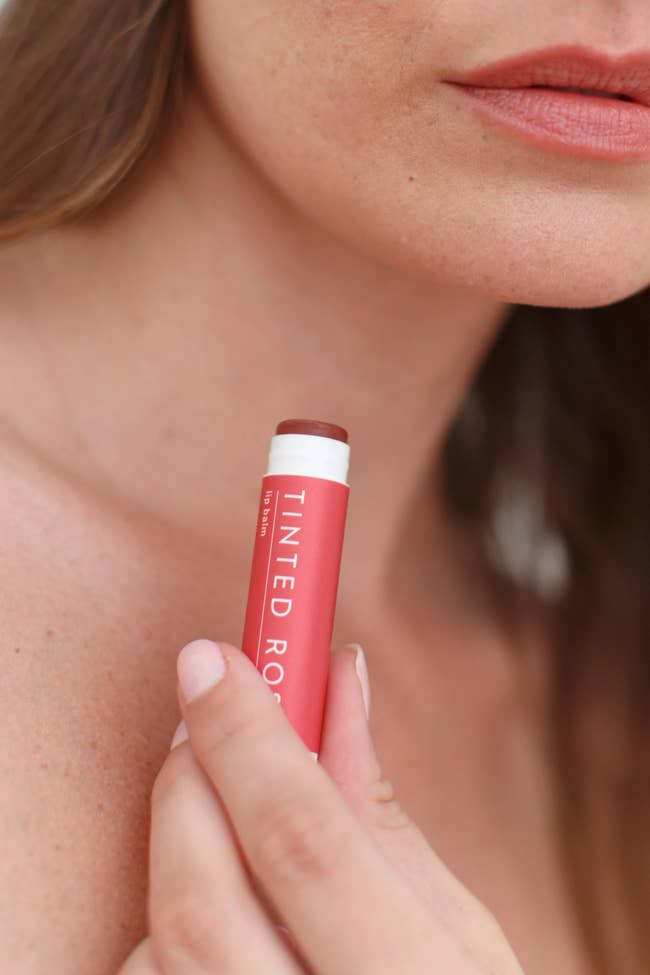 a model holding the lip balm up to their tinted lips