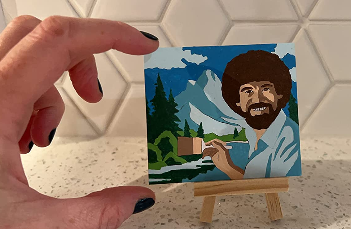 reviewer pinching their tiny painting — Bob Ross painting a landscape — to show it's smaller than their hand