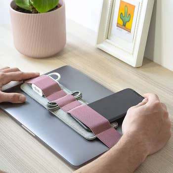 A pink elastic belt around a laptop holding a phone, a charger, and cords 