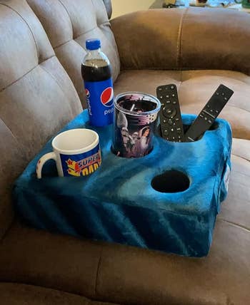 reviewer image of the cup cozy on a couch with cups and remotes in its several holders