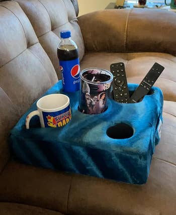 reviewer image of the cup cozy on a couch with cups and remotes in its several holders