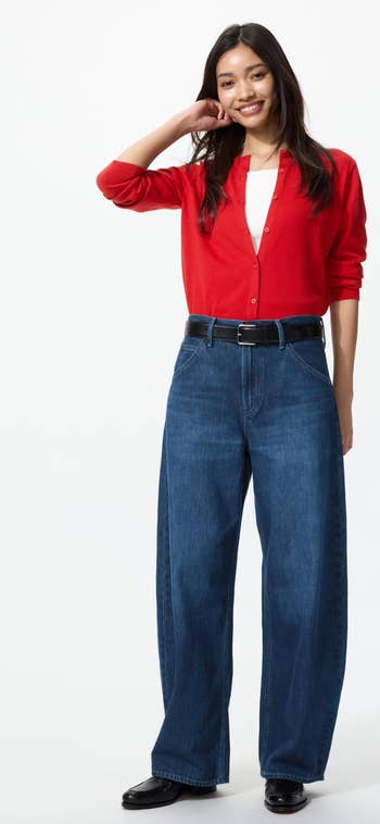 Smiling idiosyncratic   wearing a reddish  cardigan, achromatic  top, and wide-leg jeans, posing with manus  down  head