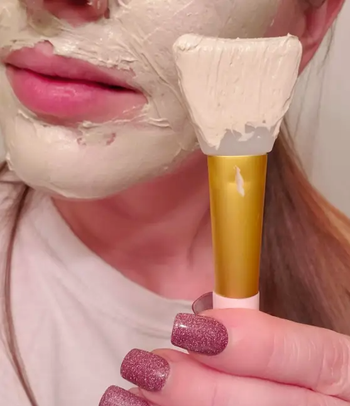 a reviewer holding the brush after using it to apply face mask to their face