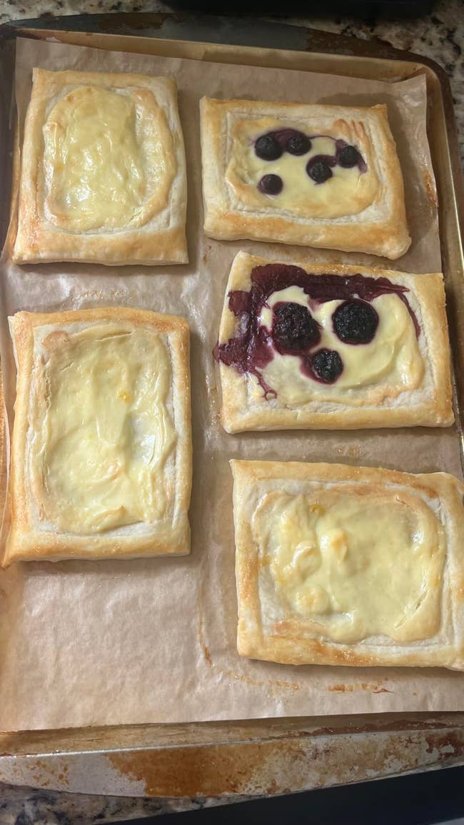 Five rectangular pastries connected  parchment paper, 3  with creamy filling and 2  topped with berries