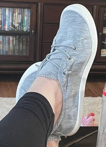 Person relaxing with their foot up, wearing a casual grey sneaker with laces 