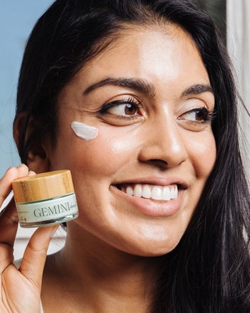 a model with eye cream under their eyes and holding the container up to their face