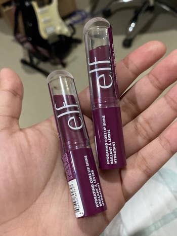 Hand holding two tubes of Elf Hydrating Core Lip Shine lip balms