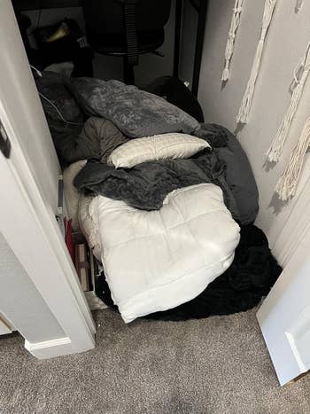 A heap  of assorted  blankets and pillows is stacked connected  the level  of a tiny  closet space, with a seat  partially disposable   successful  the background