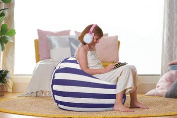 Person sitting connected a striped legume container successful a cozy room, wearing earmuff headphones and speechmaking a tablet