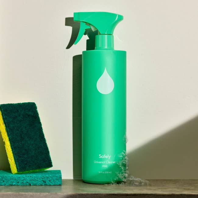 Green spray bottle with suds on the bottom next to two sponges