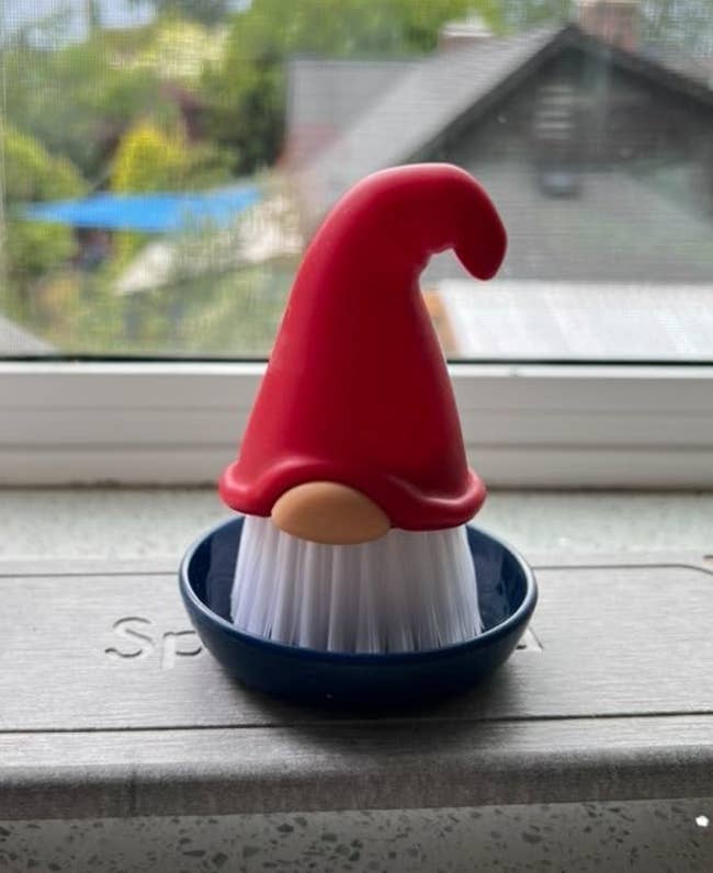 A dish brush with a red pointy gnome hat in a navy blue brush holder 