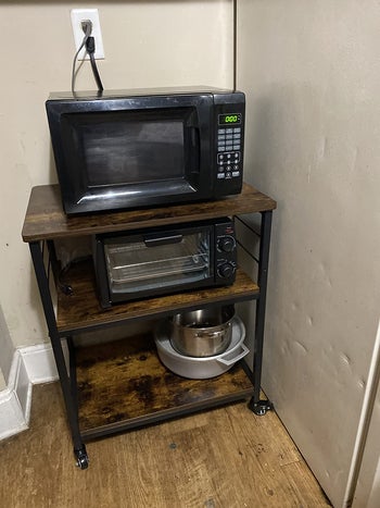 Reviewer image of brown and black wooden microwave cart with three shelves and a black microwave and toaster oven on it