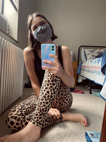 Reviewer sitting on floor in leopard print leggings and black top taking a selfie with a mask on