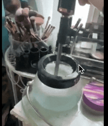 A reviewer using a small pot of soapy water to dip an electric vibrating makeup brush cleaner into 