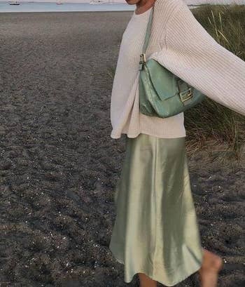 Person astatine  the formation  wearing a cozy sweater and silk skirt, holding a stylish handbag