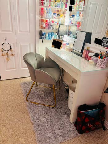 Vanity setup with shelves of quality products, a lighted reflector connected a achromatic desk, and a grey seat connected a plush rug