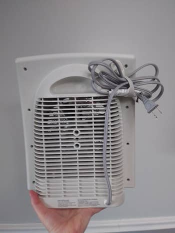 reviewer holding their abstraction  heater showing the cord bundler holding the abstraction  heater's cord neatly to the backmost  of the machine
