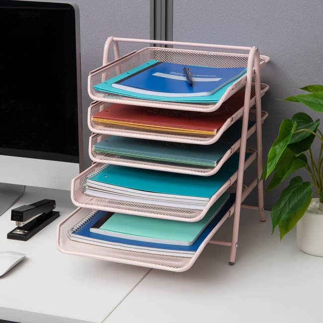 Five-tier desk organizer with assorted colorful folders on a workspace beside a computer, plant, and office supplies