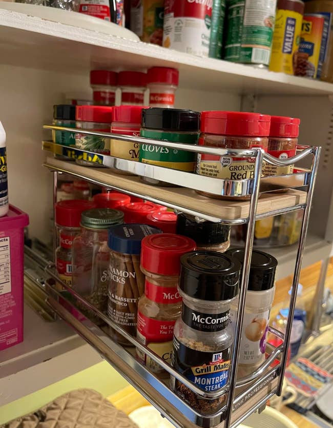 A three-tiered spice rack filled with various spice jars on a pantry shelf