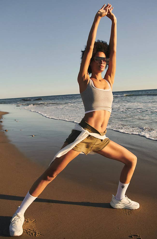 Model lunging and stretching in beige crop top and shorts on beach