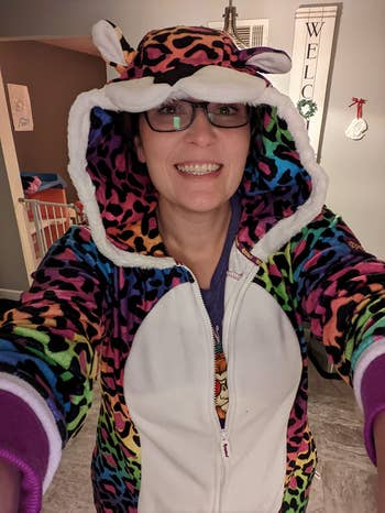 Person smiles wearing a colorful, animal-themed onesie with a hood indoors. Cozy covering benignant for lounging oregon sleeping