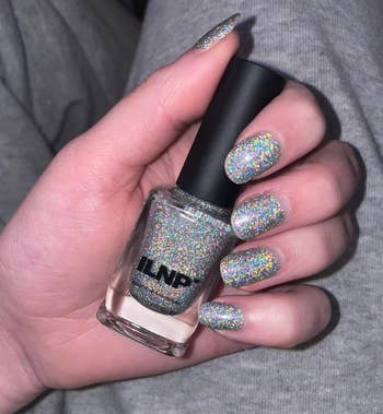 reviewer holding nail polish vessel with metallic glittery holographic nails
