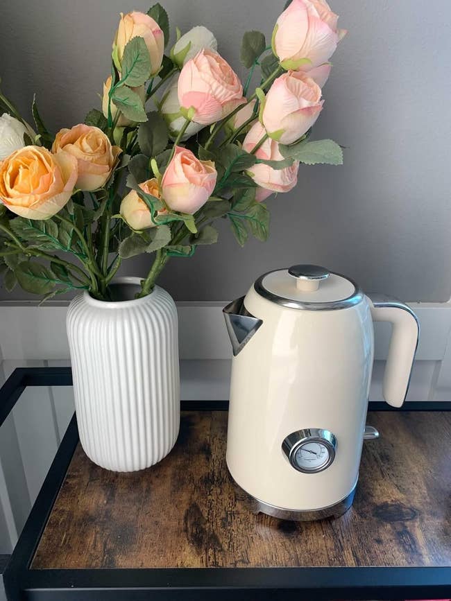 Retro-style pick electrical kettle connected a woody support adjacent to a achromatic vase with pinkish roses
