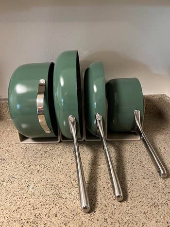 Four greenish  non-stick pans with metallic  handles are neatly stacked successful  a vertical cookware  organizer connected  a room  counter
