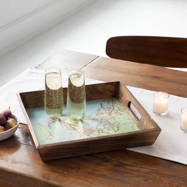 a wooden serving tray with a map design on it carrying two full champagne flutes 