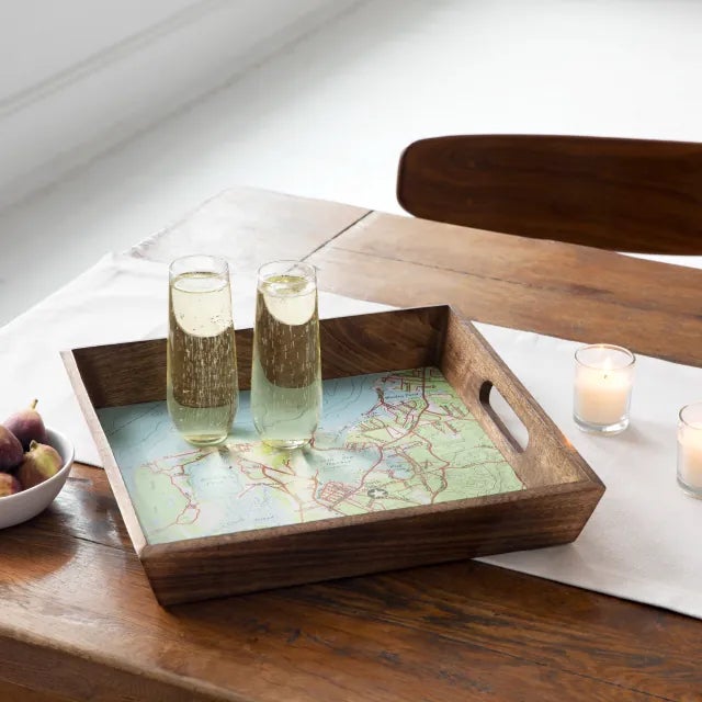 a wooden serving tray with a map design on it carrying two full champagne flutes